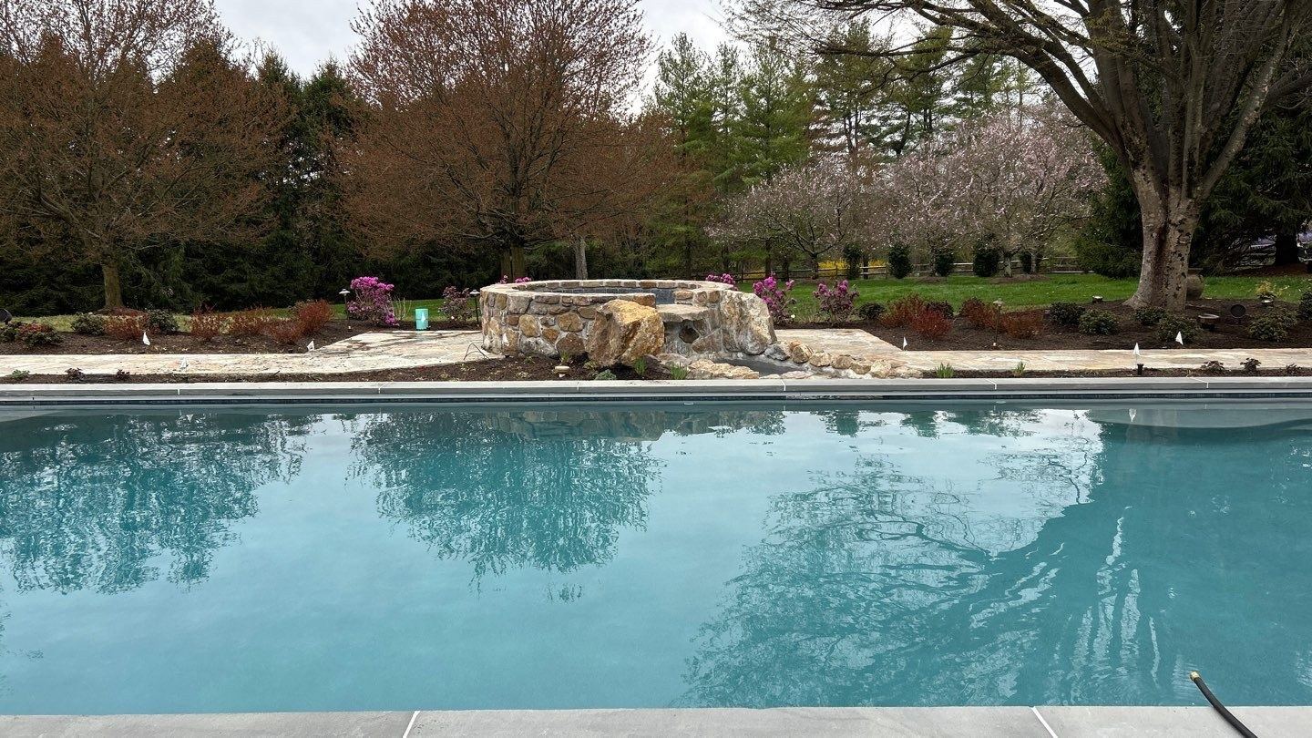 Newly finished gunite inground pool with a natural stone raised water feature and spring blossoms, built by JHL Pools in the Main Line area of PA.