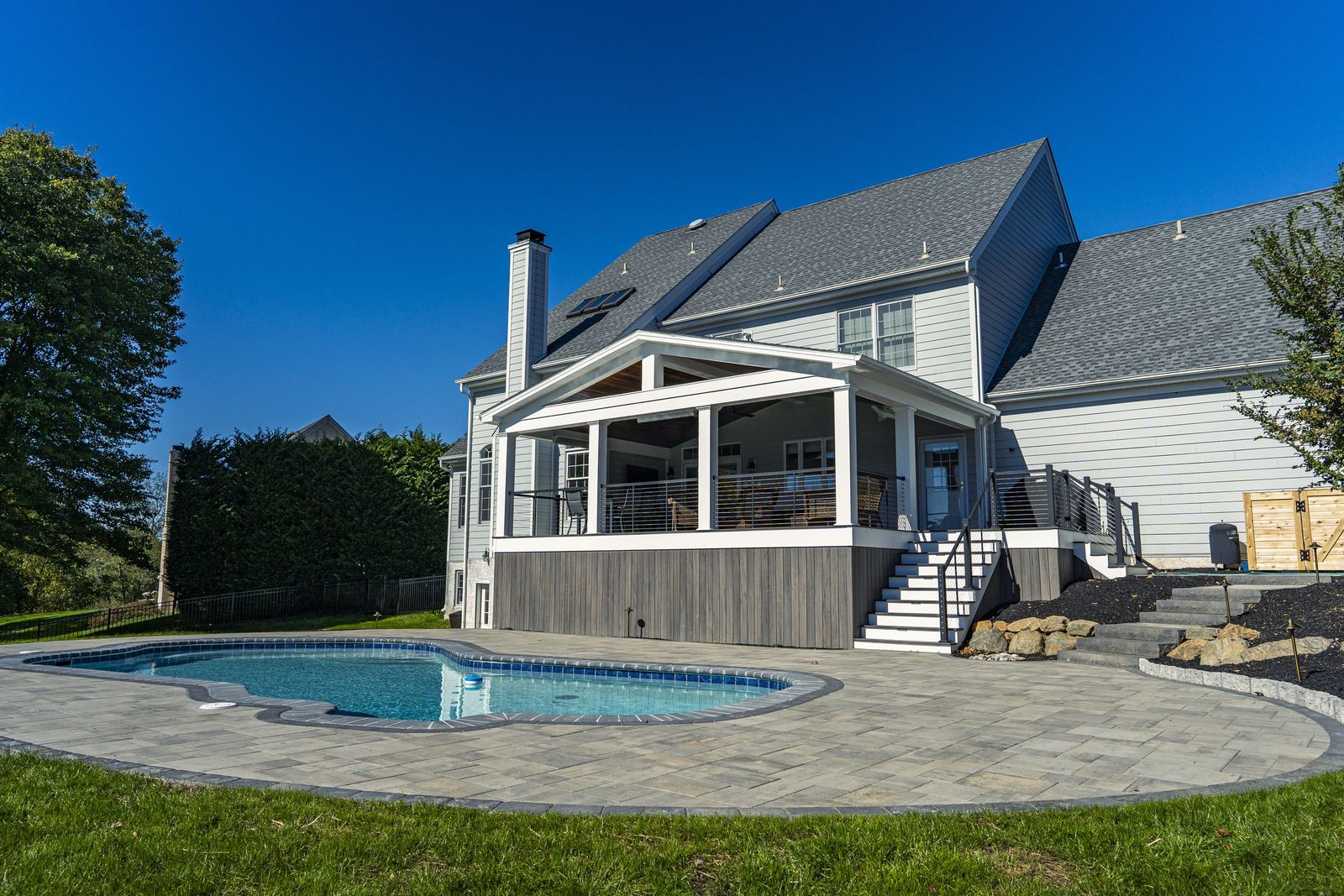 Custom freeform gunite inground pool with a tan paver patio and stone steps behind a home with a screened porch, built by JHL Pools in Newtown Square, PA.